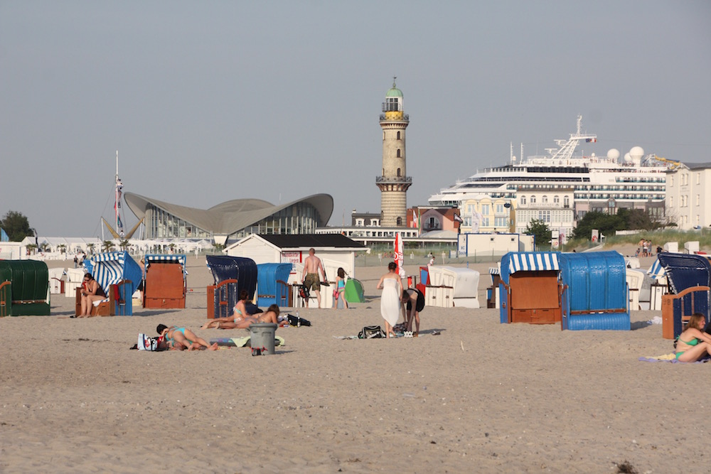 Strandkörbe, der „Teepott“ (ein legendäres und teures Strandcafé) und der alte Leuchtturm von Warnemünde.